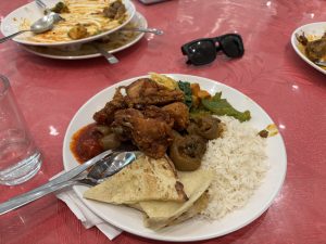 

A plate of food featuring fried chicken, rice, flatbread, green vegetables, and a tomato-based sauce.