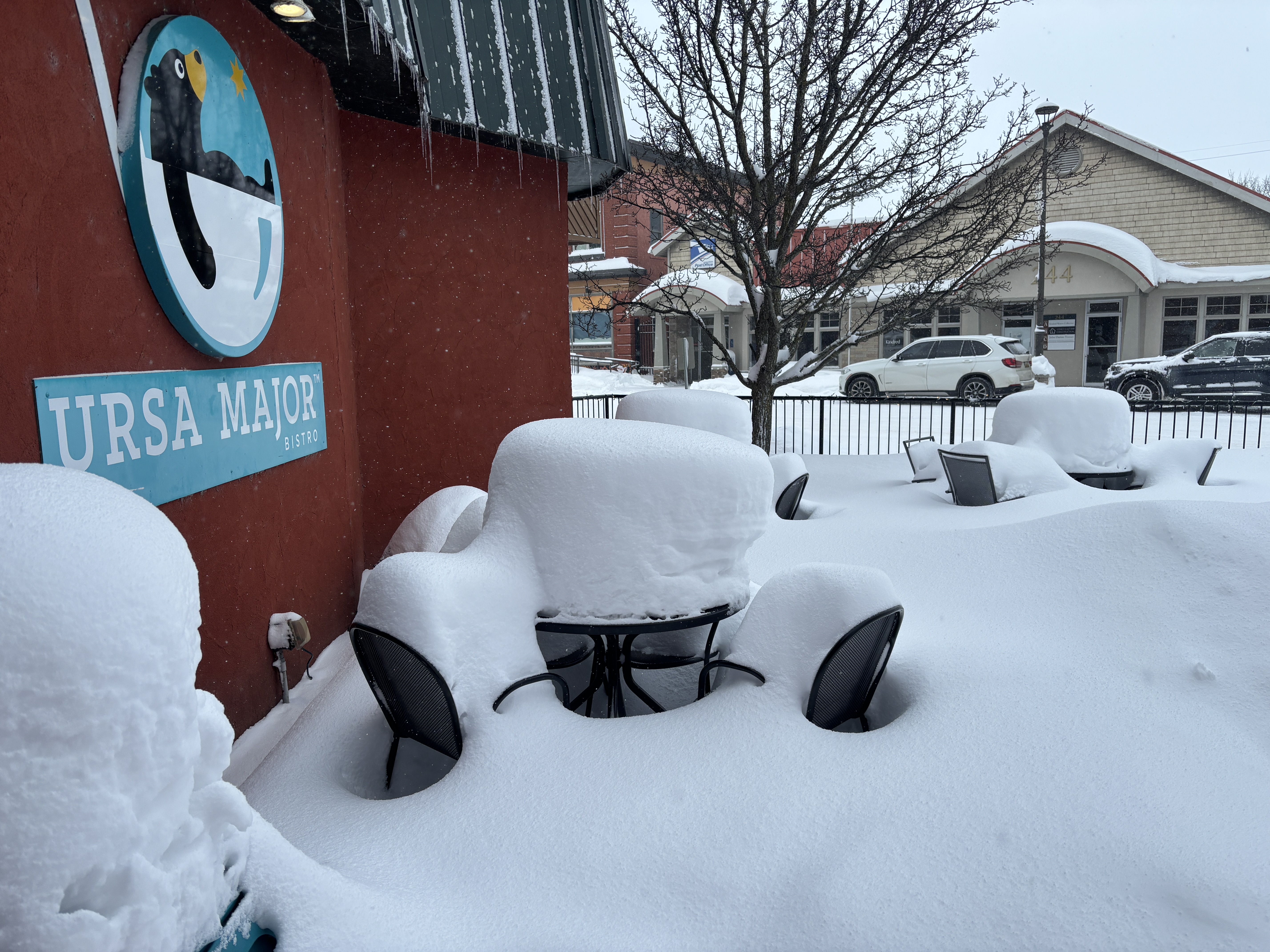 Tables covered in snow on the patio of a restaurant. The snow is approximately 90cm deep.