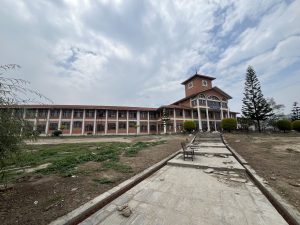 A long, multi-story building with a clock tower in the center is surrounded by a sparse landscape