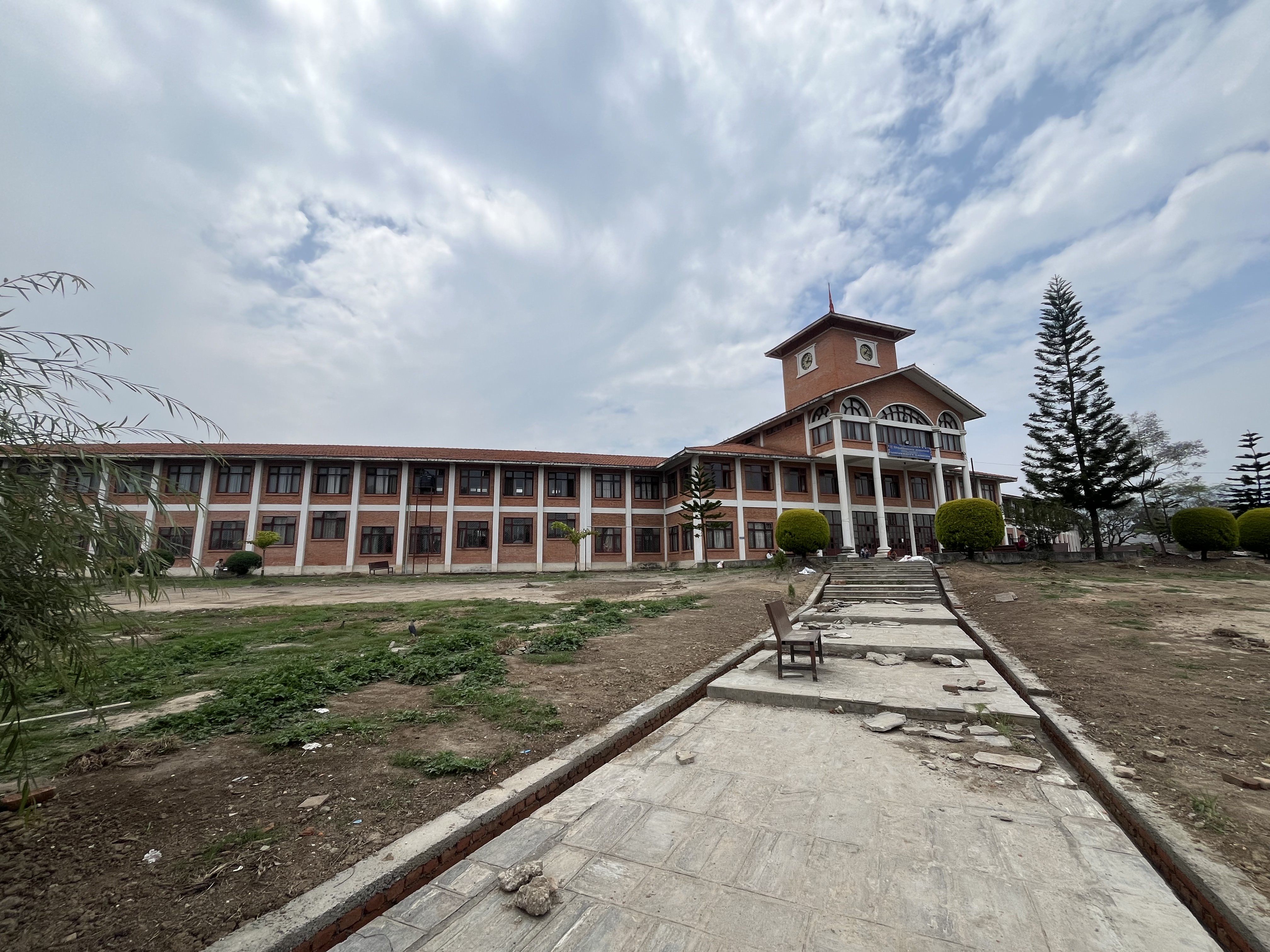 A long, multi-story building with a clock tower in the center is surrounded by a sparse landscape