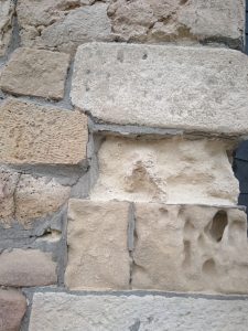 A close-up view of a textured stone wall featuring a variety of stones in different shapes and colors, including light beige, gray, and hints of pink.