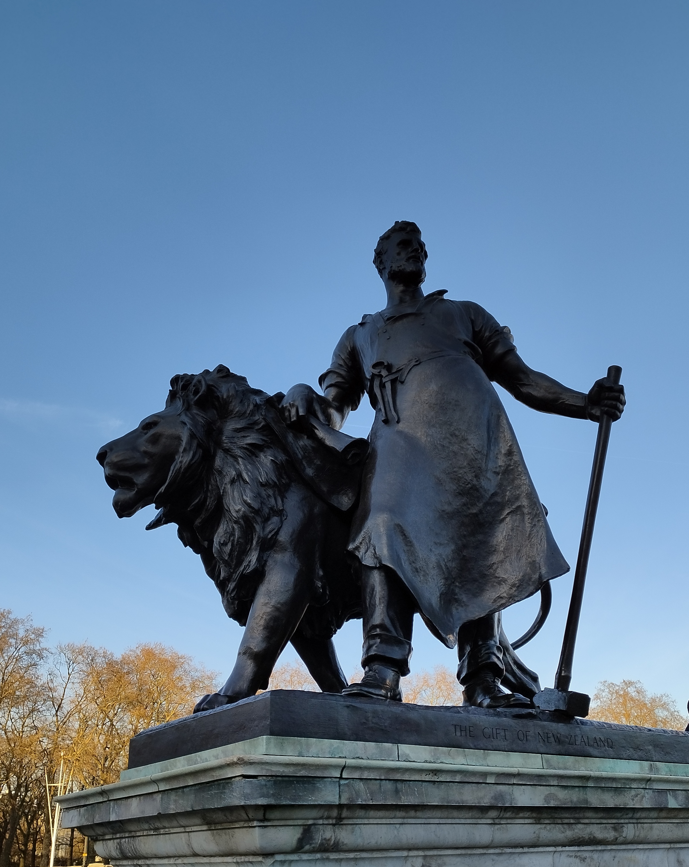 A bronze statue depicting a man with a beard, wearing a long apron, holding a staff in his right hand.