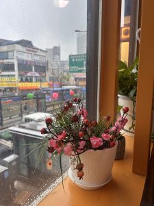 A close-up of a decorative flower pot filled with artificial flowers sits on a windowsill.