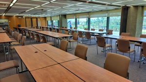 A spacious conference room featuring several rows of rectangular tables arranged for meetings, with beige chairs positioned around them. 