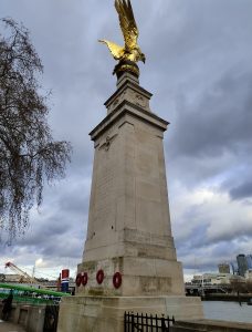 A tall stone monument with a golden eagle perched on top, standing against a cloudy sky. 