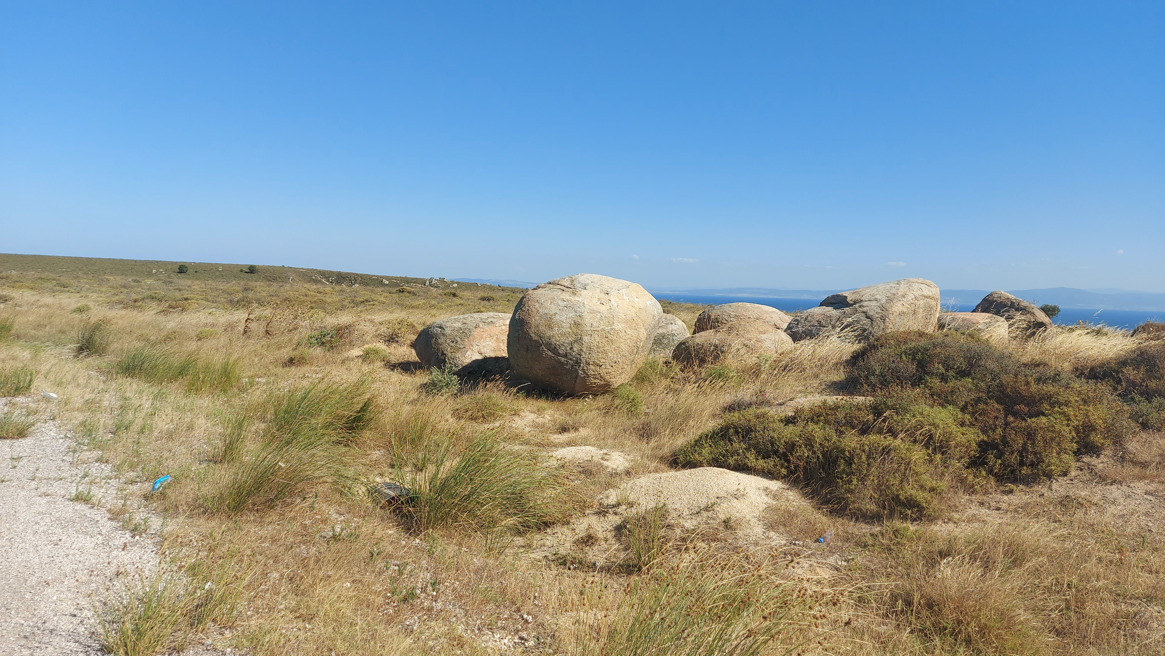 A landscape with large rounded boulders scattered across dry, grassy terrain under a clear blue sky.