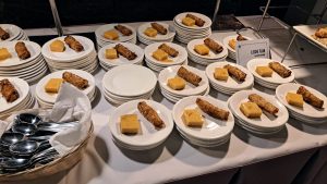 A table with several stacks of white plates, each containing a piece of leche flan and a crispy rolled dessert, resembling spring rolls.