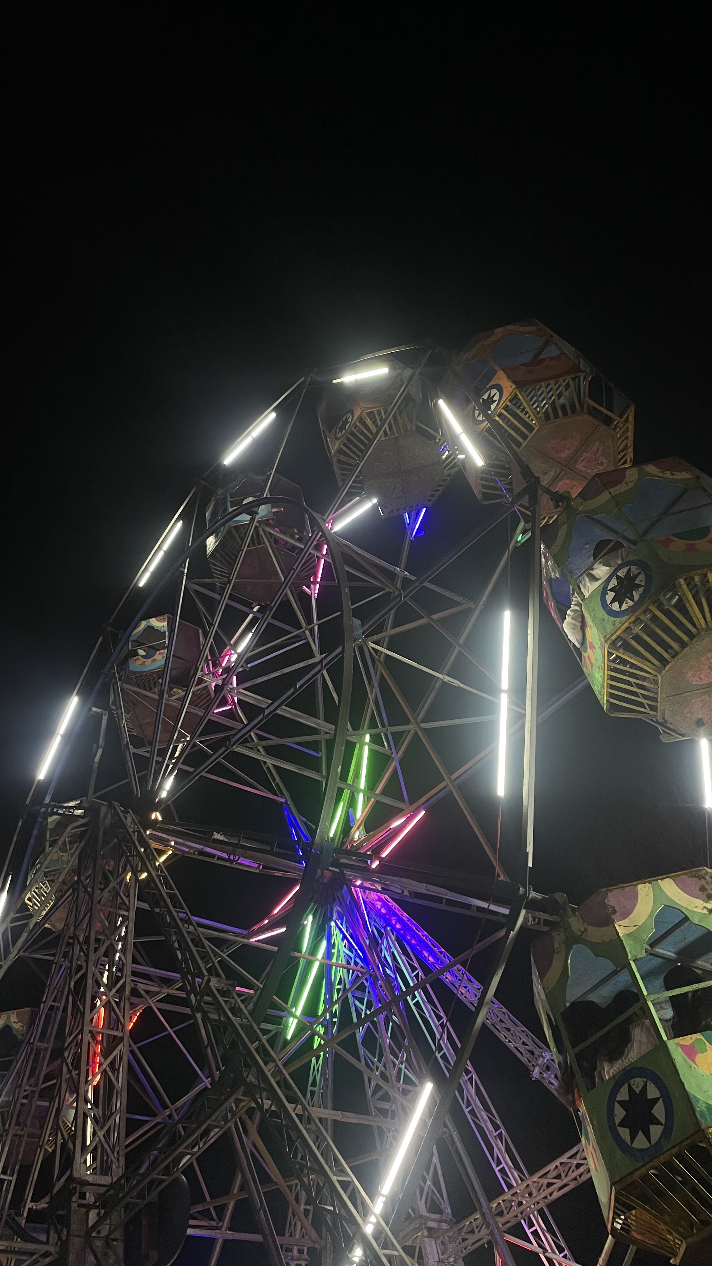 A ferris wheel lit up at night with round, cage-like cars brightly colored.