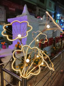 A decorative installation featuring illuminated wire flowers with glowing outlines and central bulbs, set against a backdrop of a white stone-like structure. 