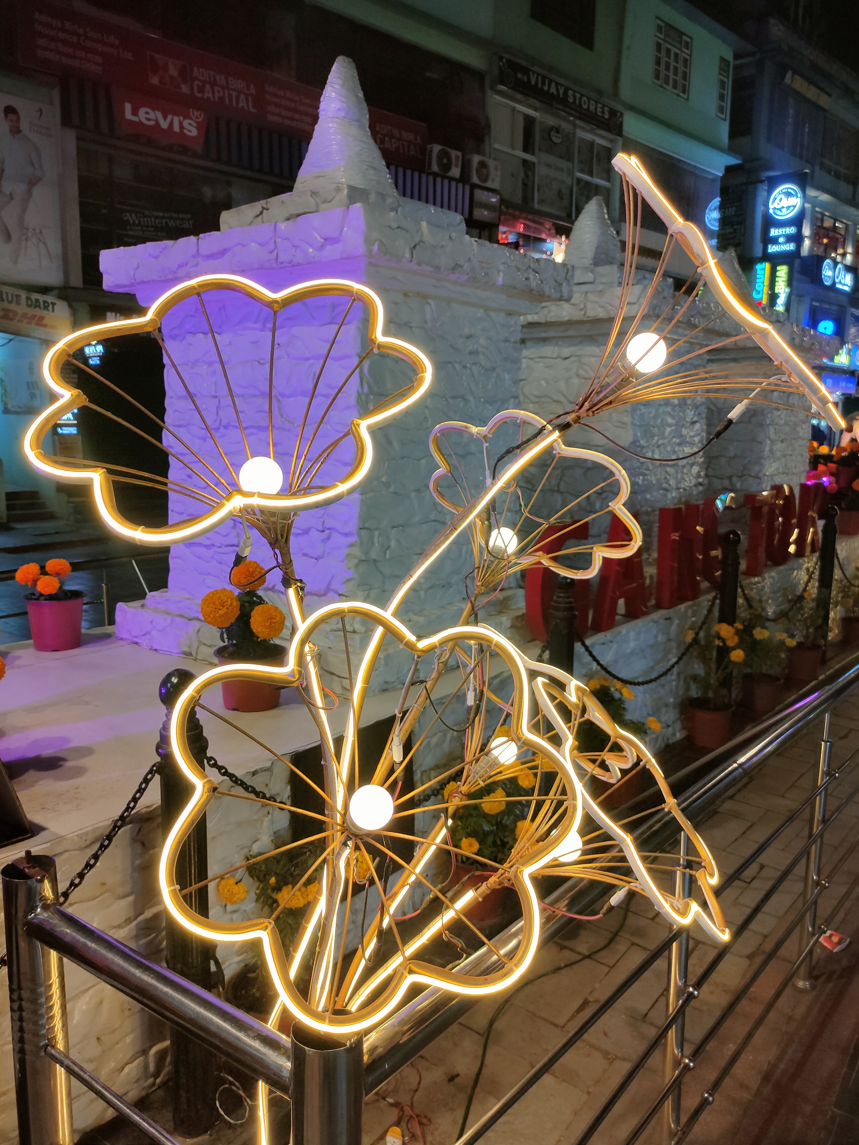 A decorative installation featuring illuminated wire flowers with glowing outlines and central bulbs, set against a backdrop of a white stone-like structure.