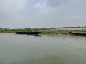 A calm river with two long, narrow boats near a grassy riverbank under a partly cloudy sky.

