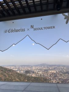 A panoramic view of a cityscape can be seen through a large glass window, featuring the silhouettes of mountains in the background.