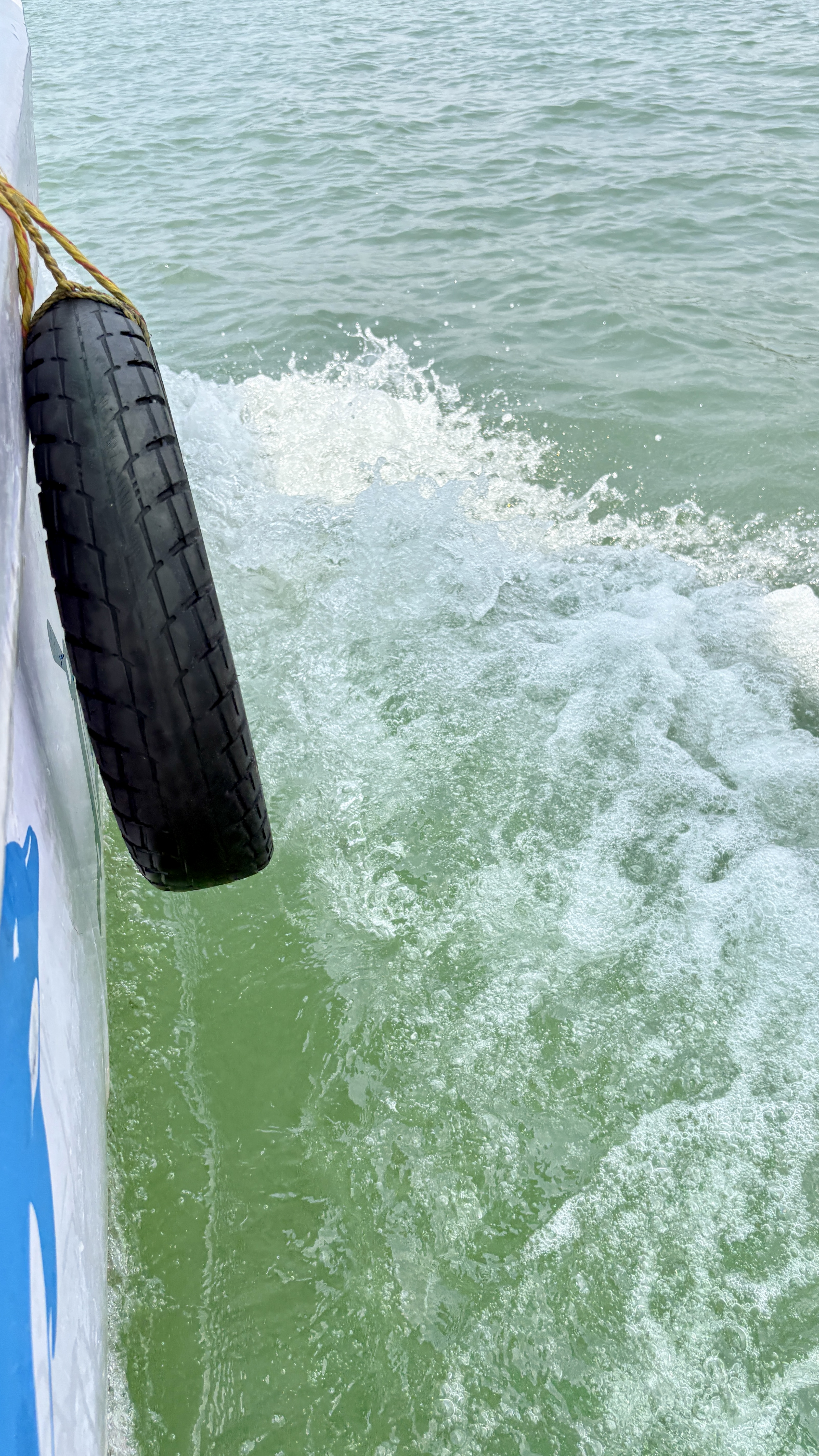 A close-up view of water splashing around a black tire hanging from the side of a boat