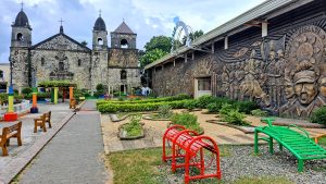 Mural wall depecting a local tradition with a centuries old church, surrounded with small landscaped garden and children's playground.