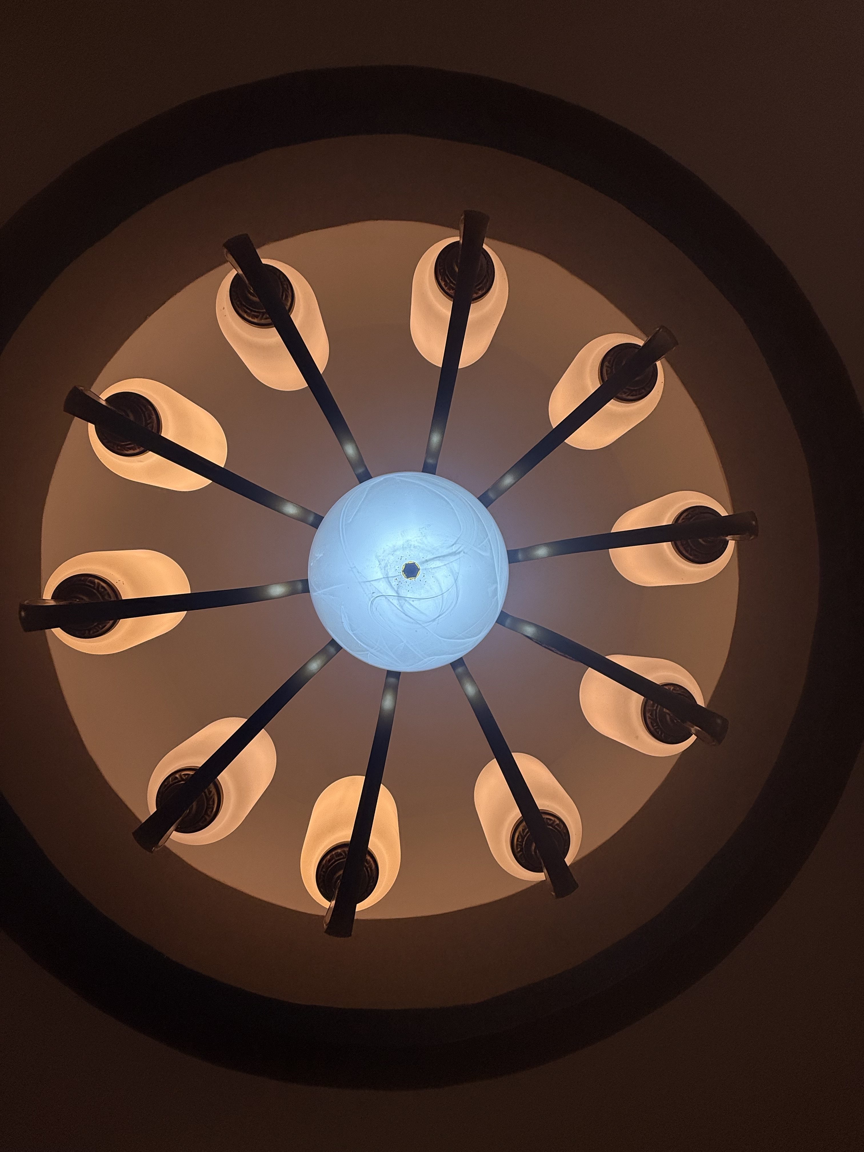 A circular chandelier with a central blue light surrounded by eight soft white lights, viewed from below against a dark background.