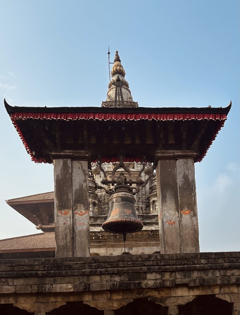 Ornate stone structure with a large hanging bell at Bhaktapur Durbar Square.
