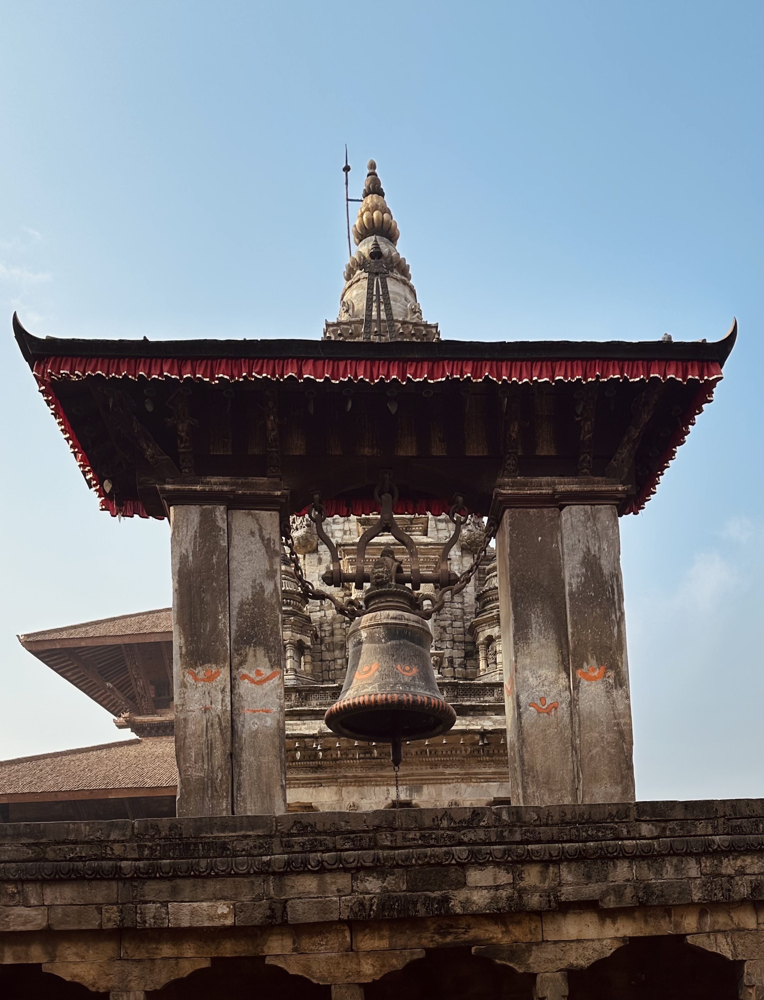Ornate stone structure with a large hanging bell at Bhaktapur Durbar Square.