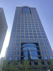 A tall, modern skyscraper is depicted, showcasing a glass and stone facade with a grid pattern of square windows