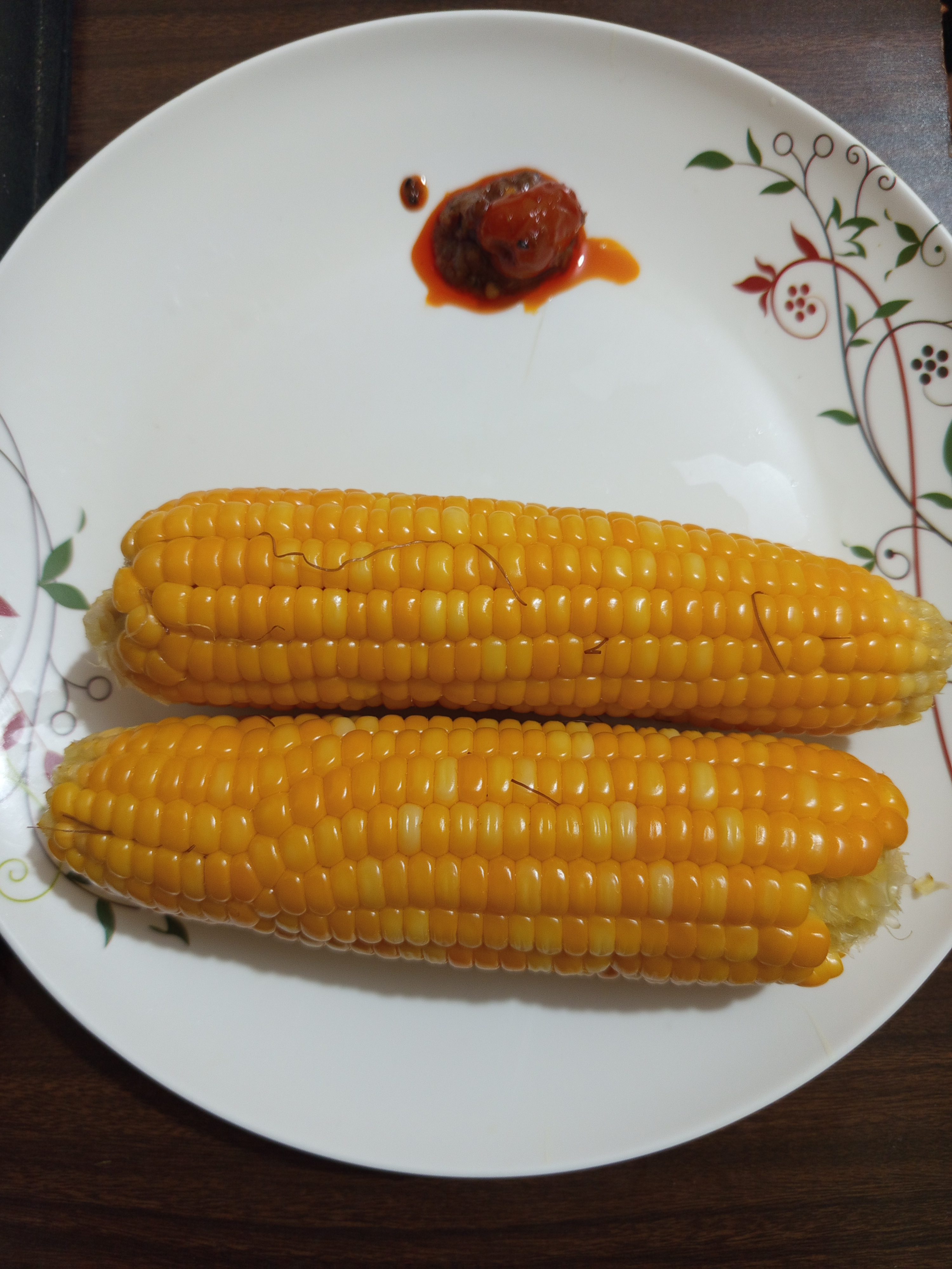 Two ears of corn on the cob placed on a white decorative plate with a small serving of sauce or condiment.