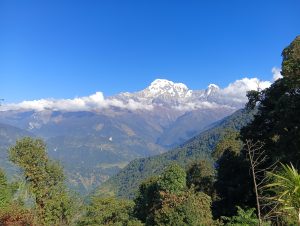A breathtaking view of snow-capped mountains under a clear blue sky, with fluffy white clouds hovering over the peaks.