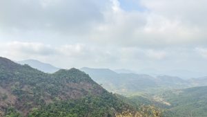 A panoramic view of lush, green hills and mountains under a partly cloudy sky.