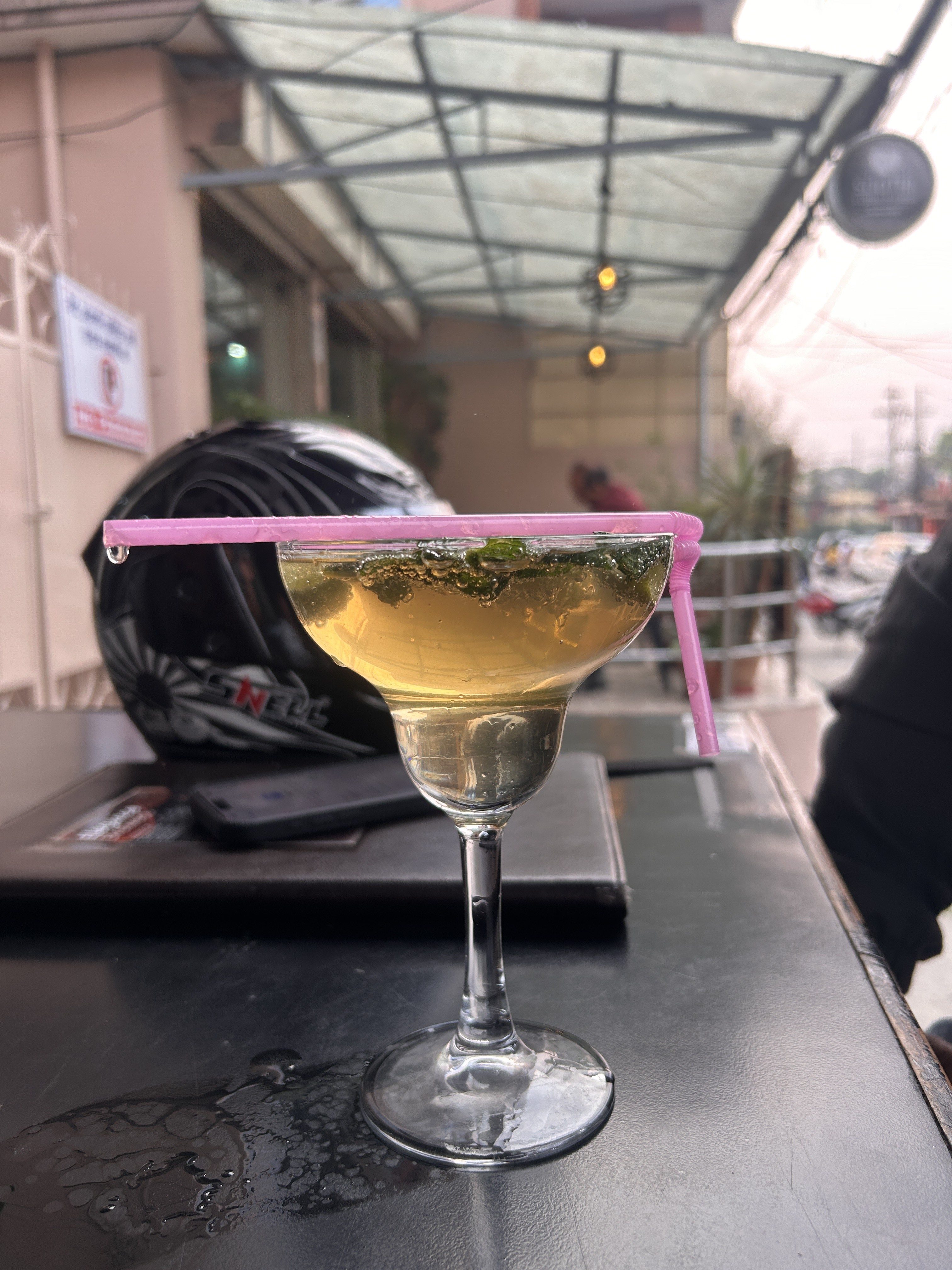 A close-up of a cocktail glass filled with a light-colored drink, garnished with mint leaves, and a pink straw resting on the rim.