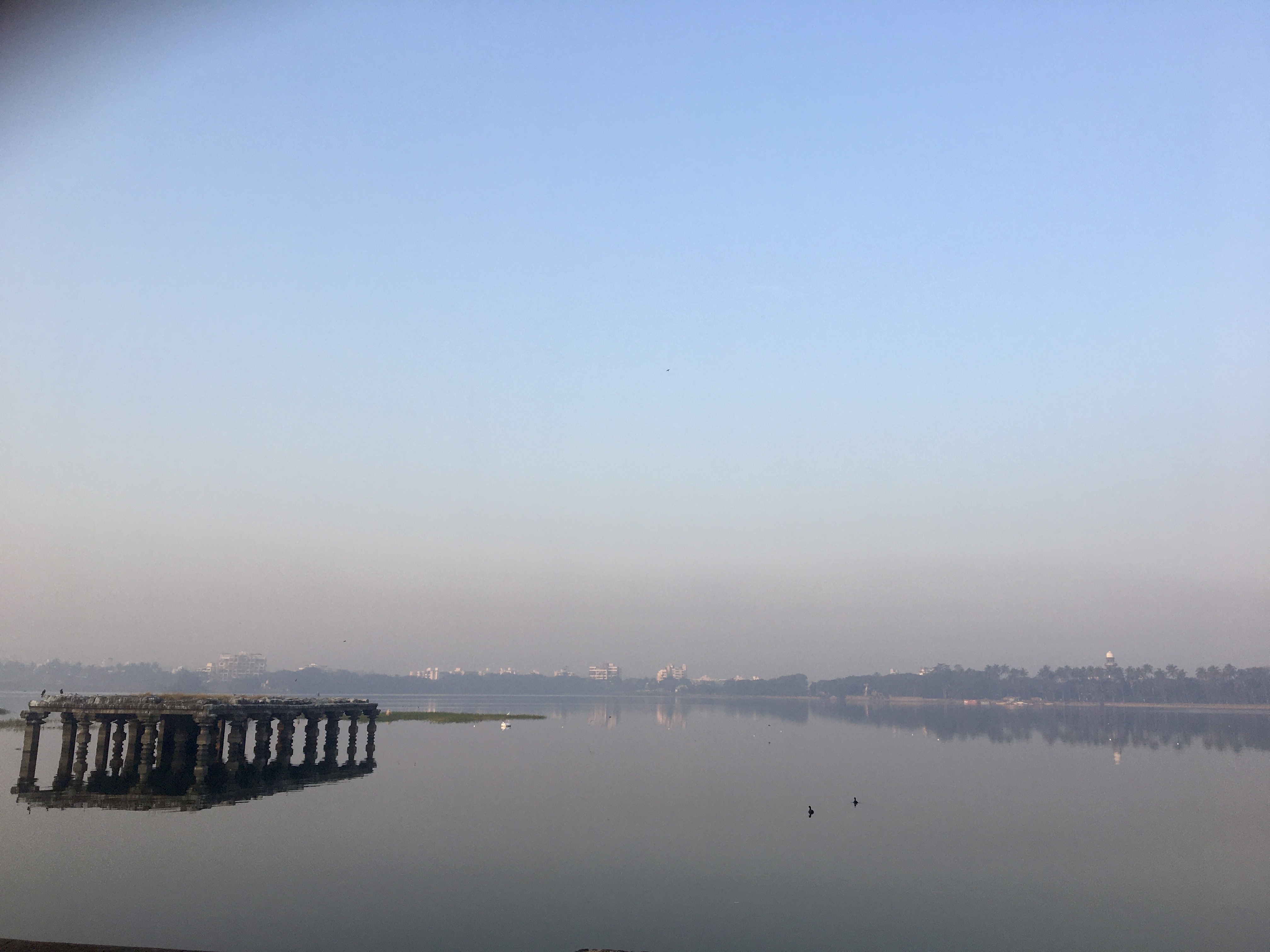 Serene early morning view of a calm lake with an ancient stone pavilion structure partially submerged in the water.