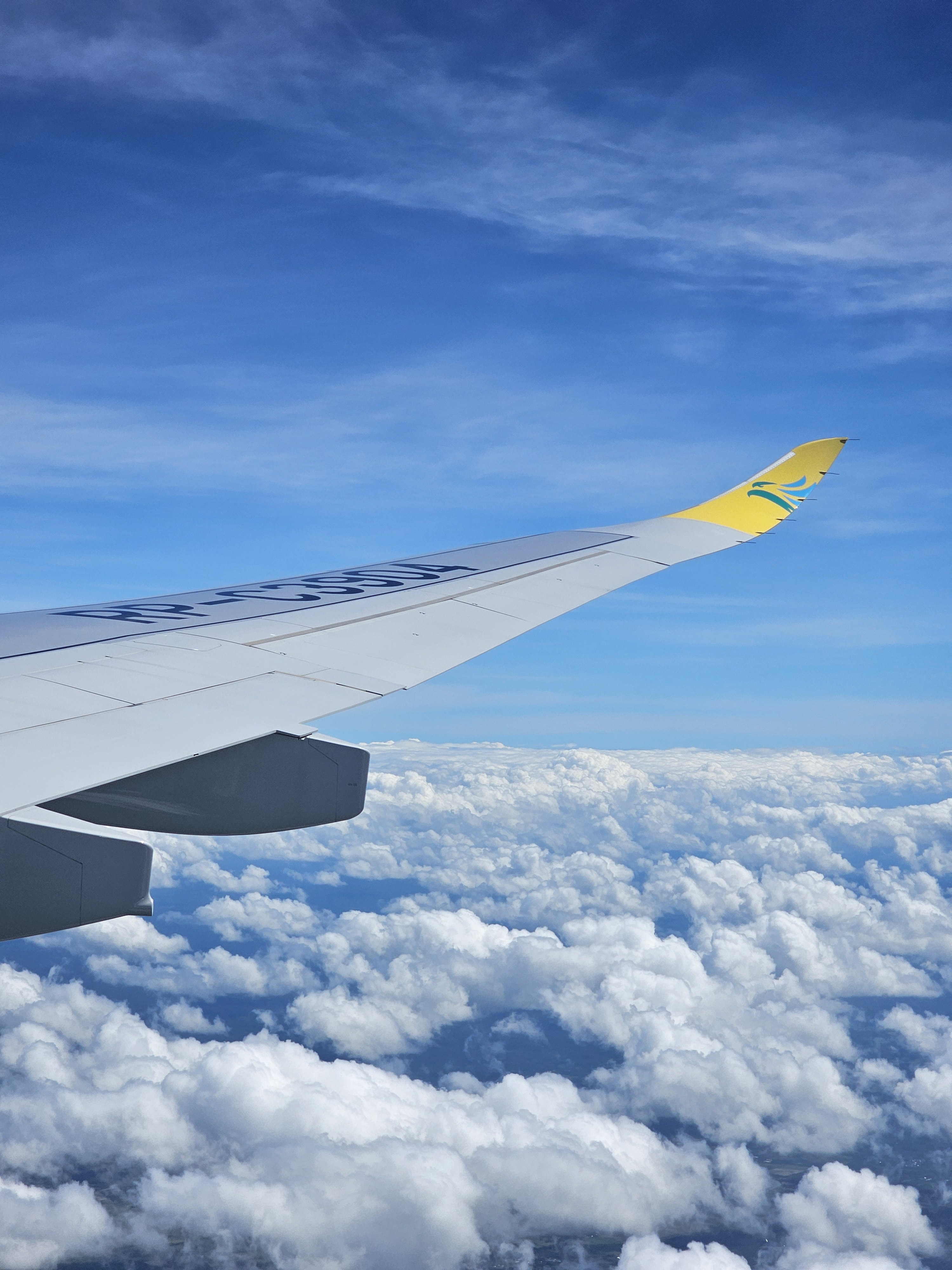 View from an airplane window showing the wing against a backdrop of fluffy white clouds and a clear blue sky.