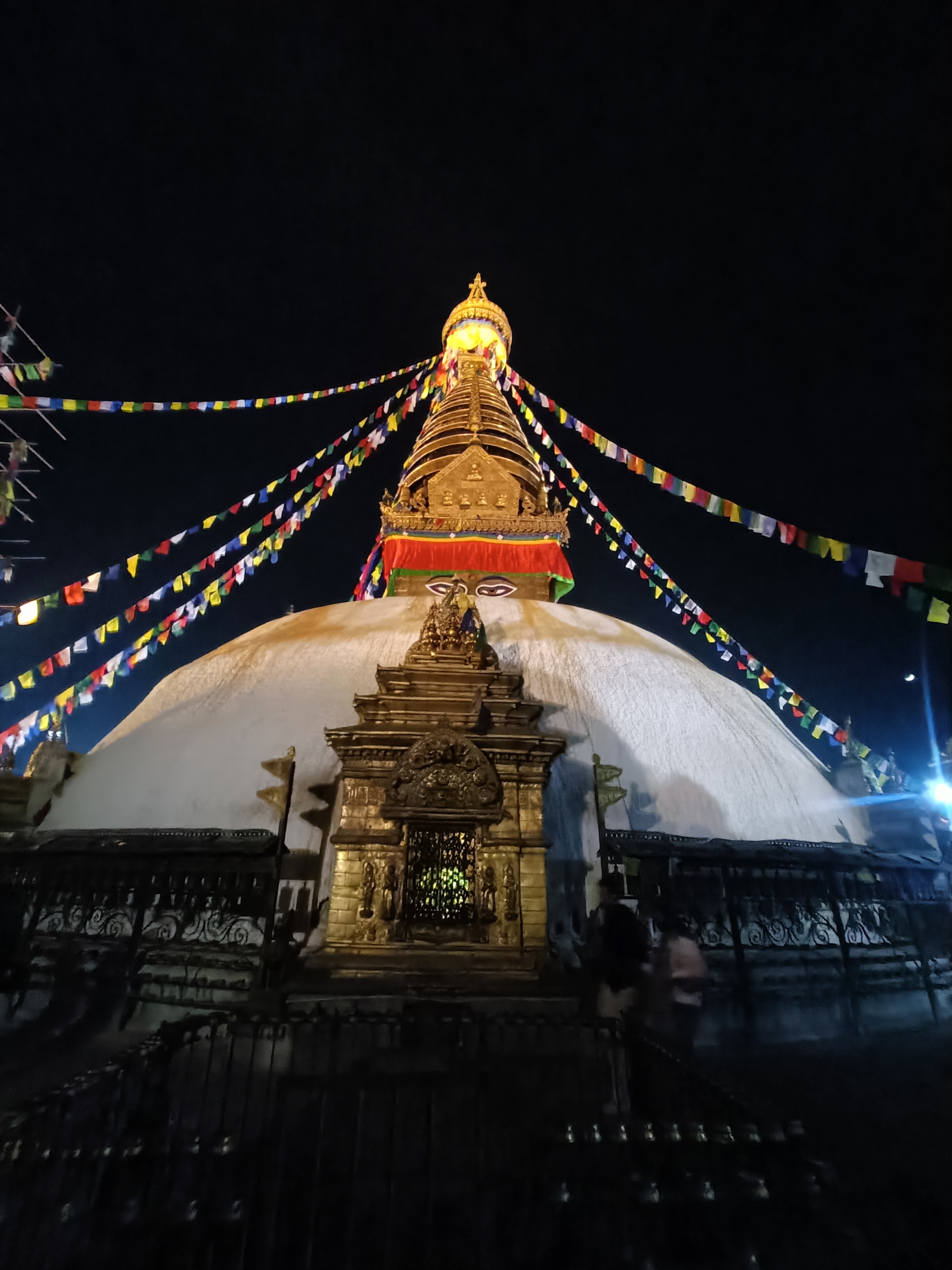 A large stupa illuminated at night, featuring a golden spire at the top.