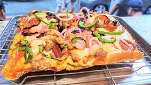 A freshly baked pizza on a metal cooling rack, topped with a variety of ingredients including slices of pepperoni, green bell peppers, onions, mushrooms, and pieces of sausage