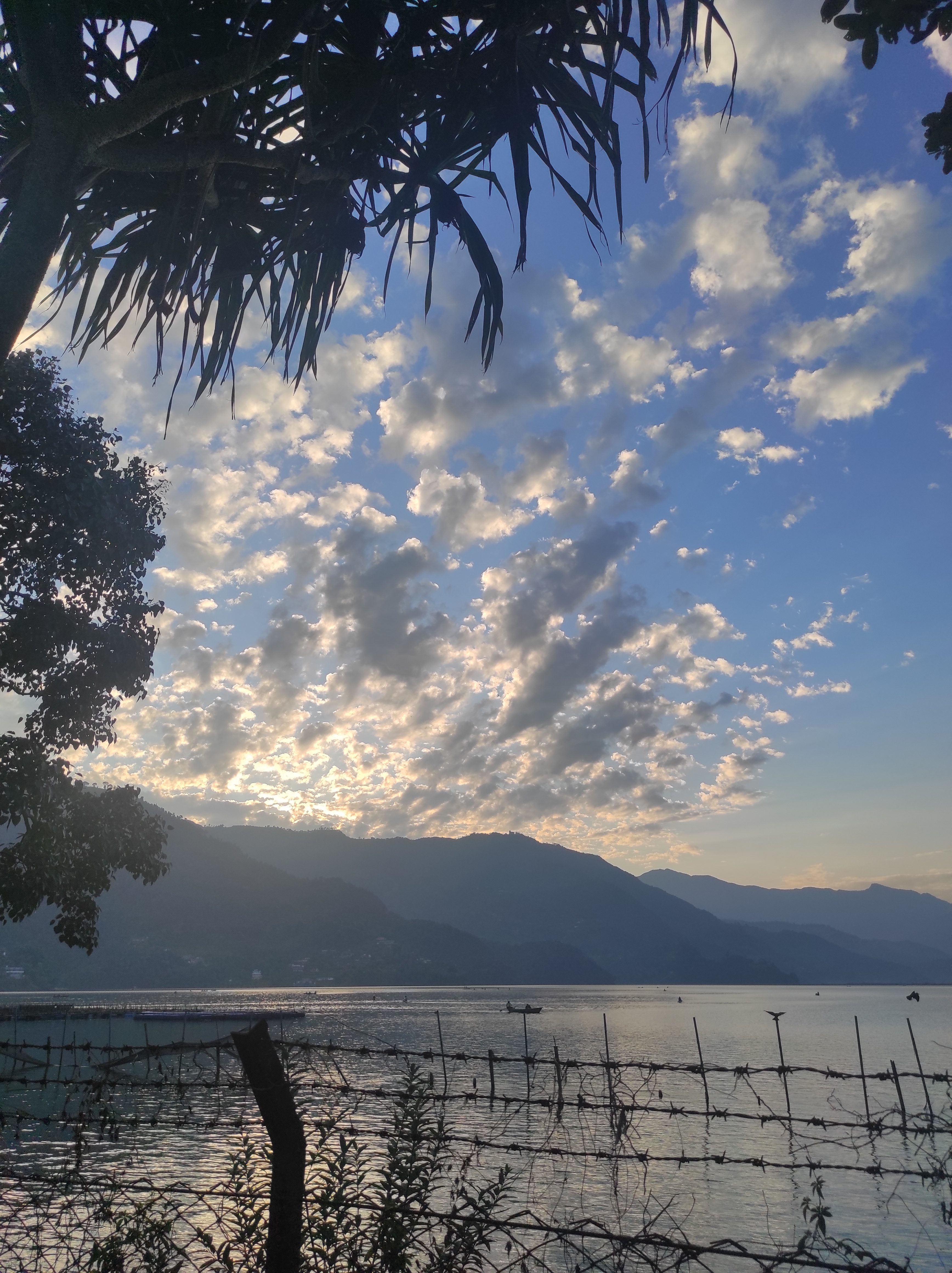 A tranquil lakeside scene during sunset, featuring dramatic clouds illuminated by the fading light.