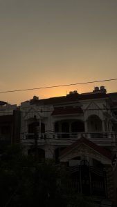 A silhouette of a two-story house with ornate details is seen against a sunset sky. 
