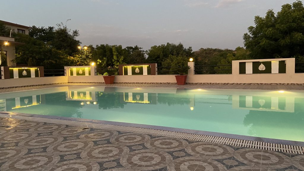 A serene outdoor swimming pool surrounded by a stylish tiled deck, illuminated by warm lights.