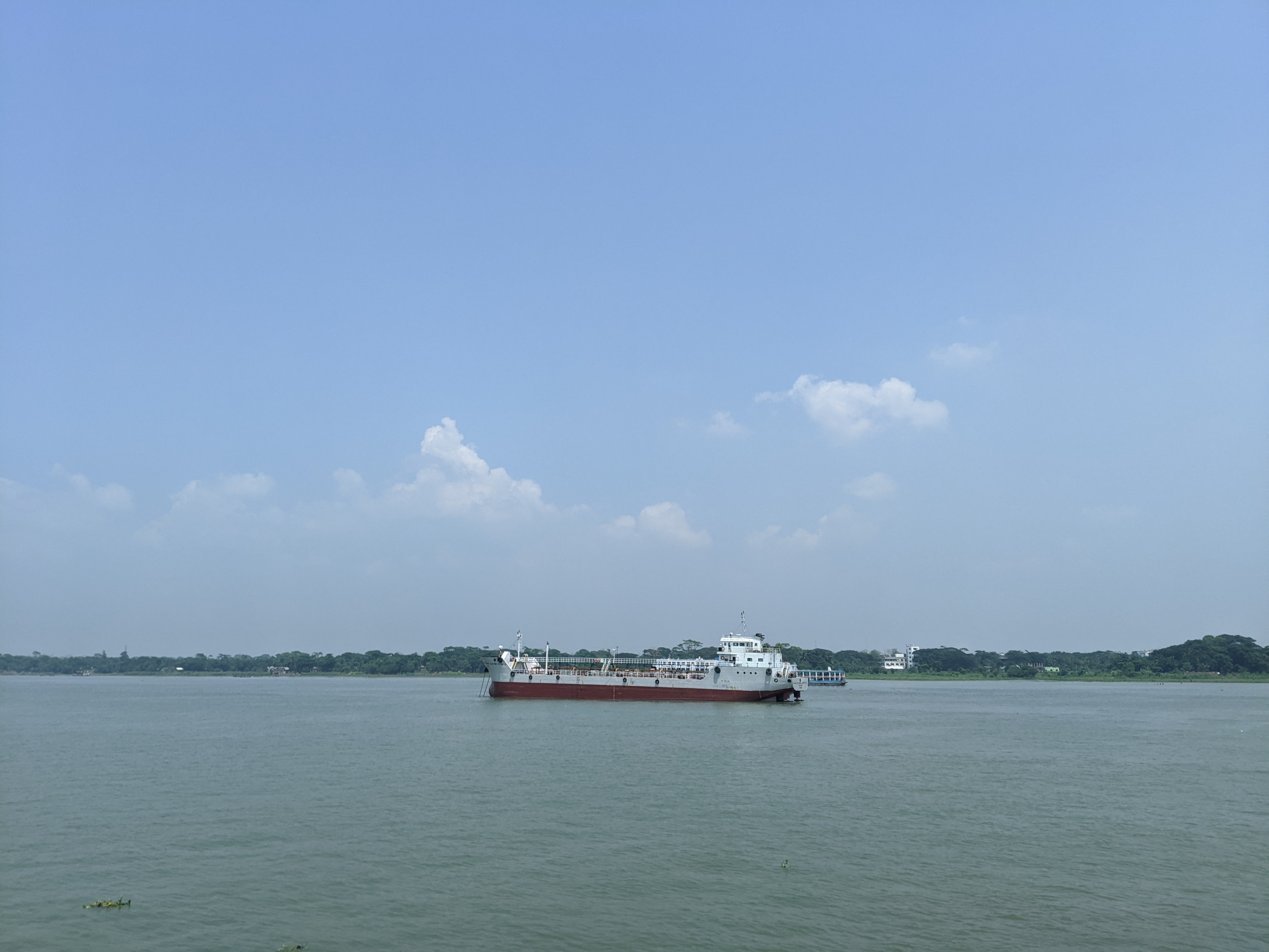 A large ship is cruising in a calm body of water under a clear blue sky with a few fluffy white clouds.