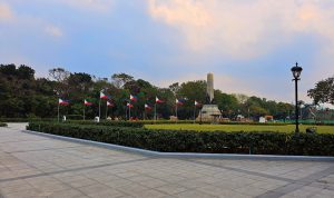 A wide view of a park featuring several Philippine flags planted along a pathway. 
