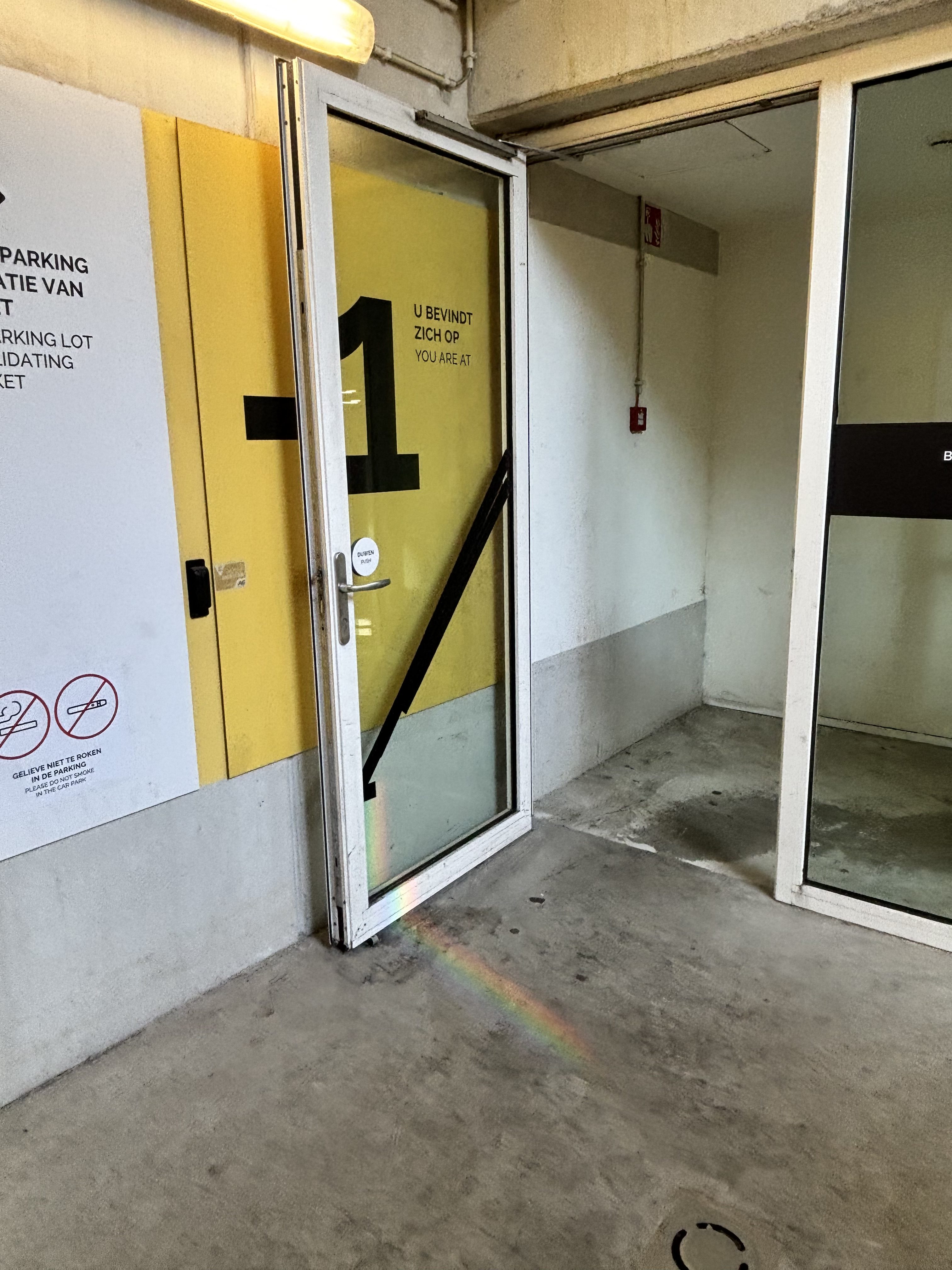A serene scene from a parking lot, where sunlight reflects off a glass door, casting a soft rainbow across the surface.