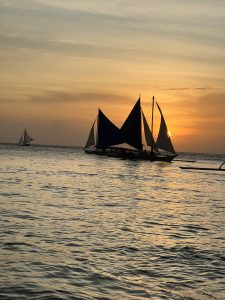  A tranquil sunset over the ocean in Boracay, Philippines, with two sailboats silhouetted against the colorful sky.
