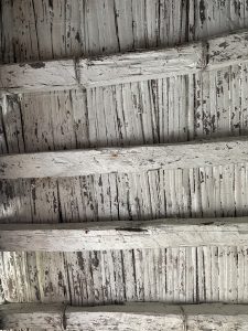 Textured ceiling with wooden beams. The beams are painted white and are slightly rough with visible paint wear and aging. 