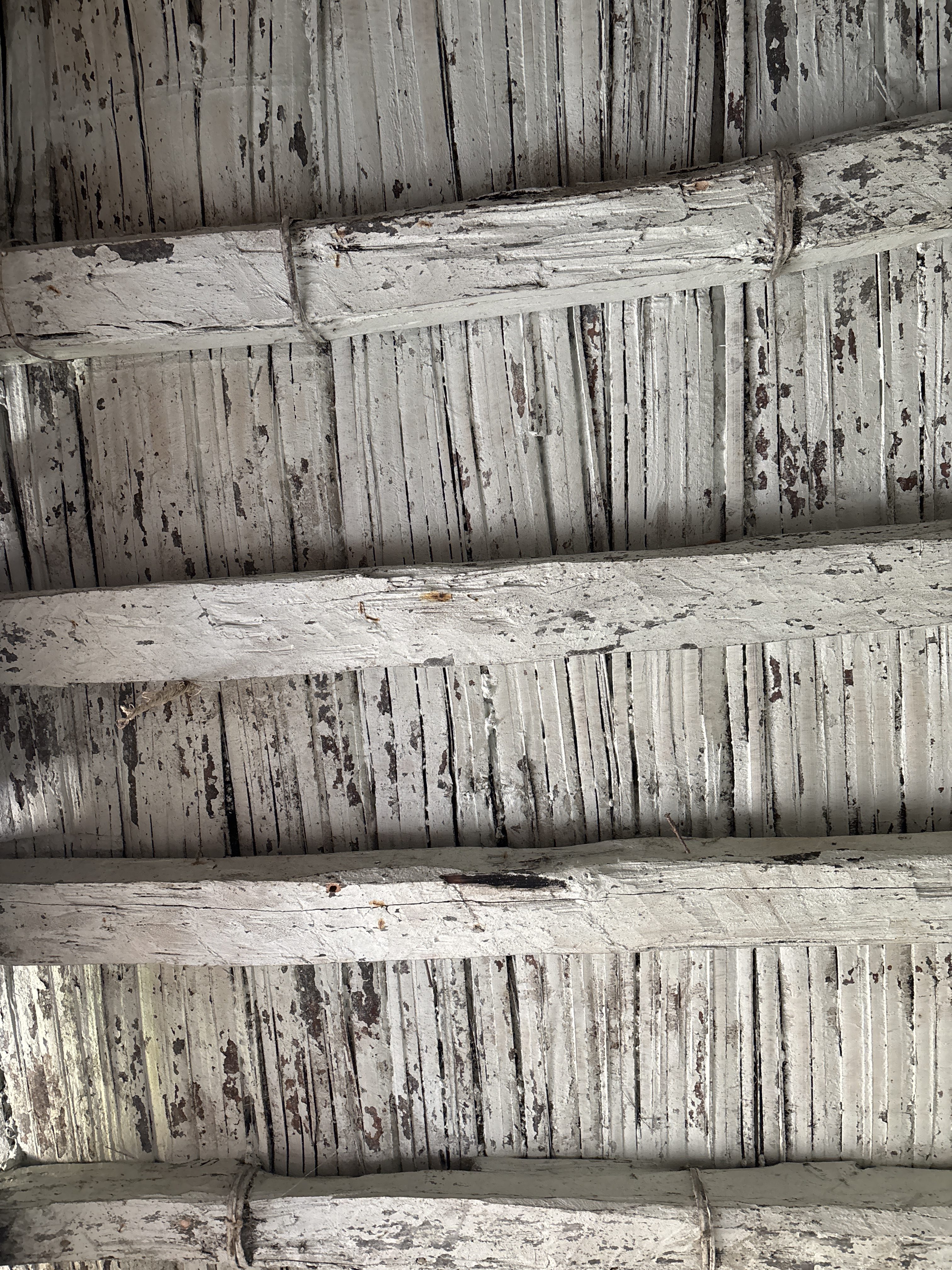 Textured ceiling with wooden beams. The beams are painted white and are slightly rough with visible paint wear and aging.