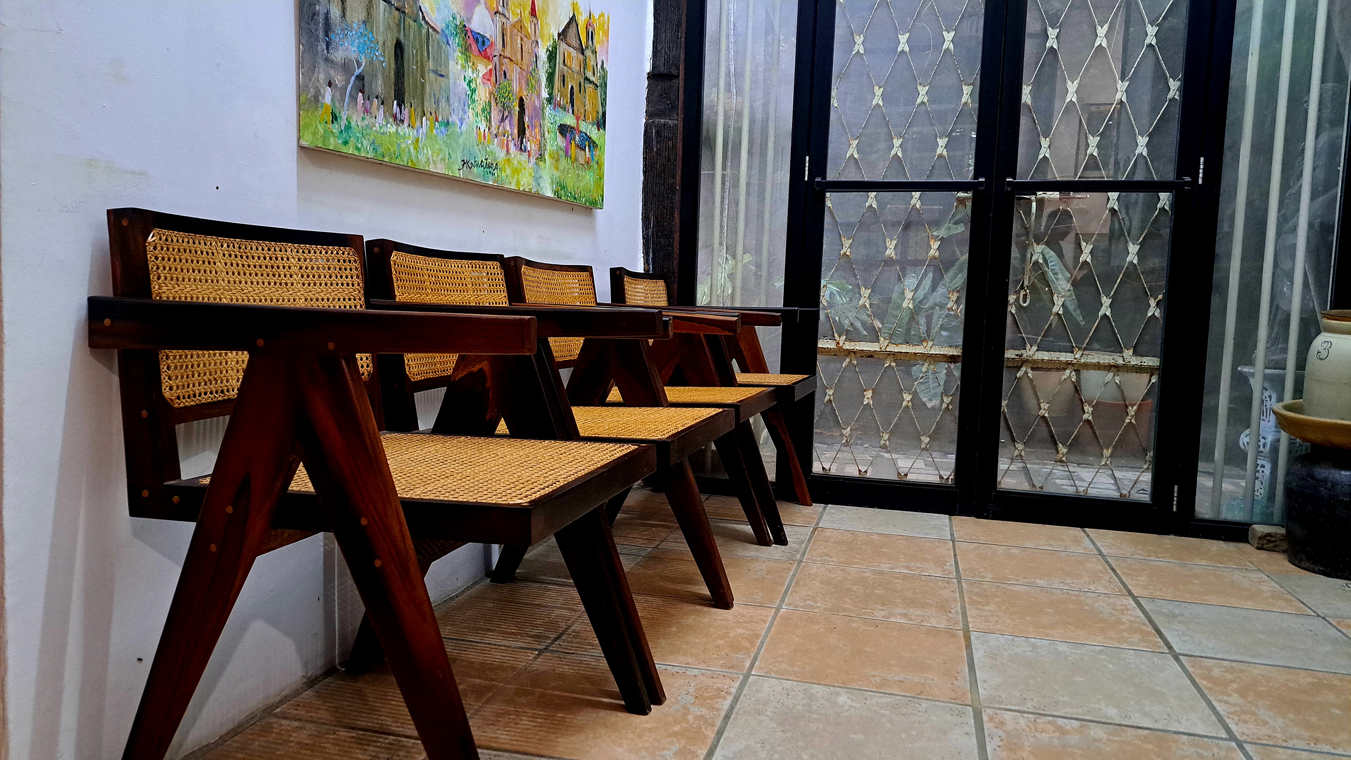 A cozy corner featuring a row of four wooden chairs with cane seats arranged against a white wall.