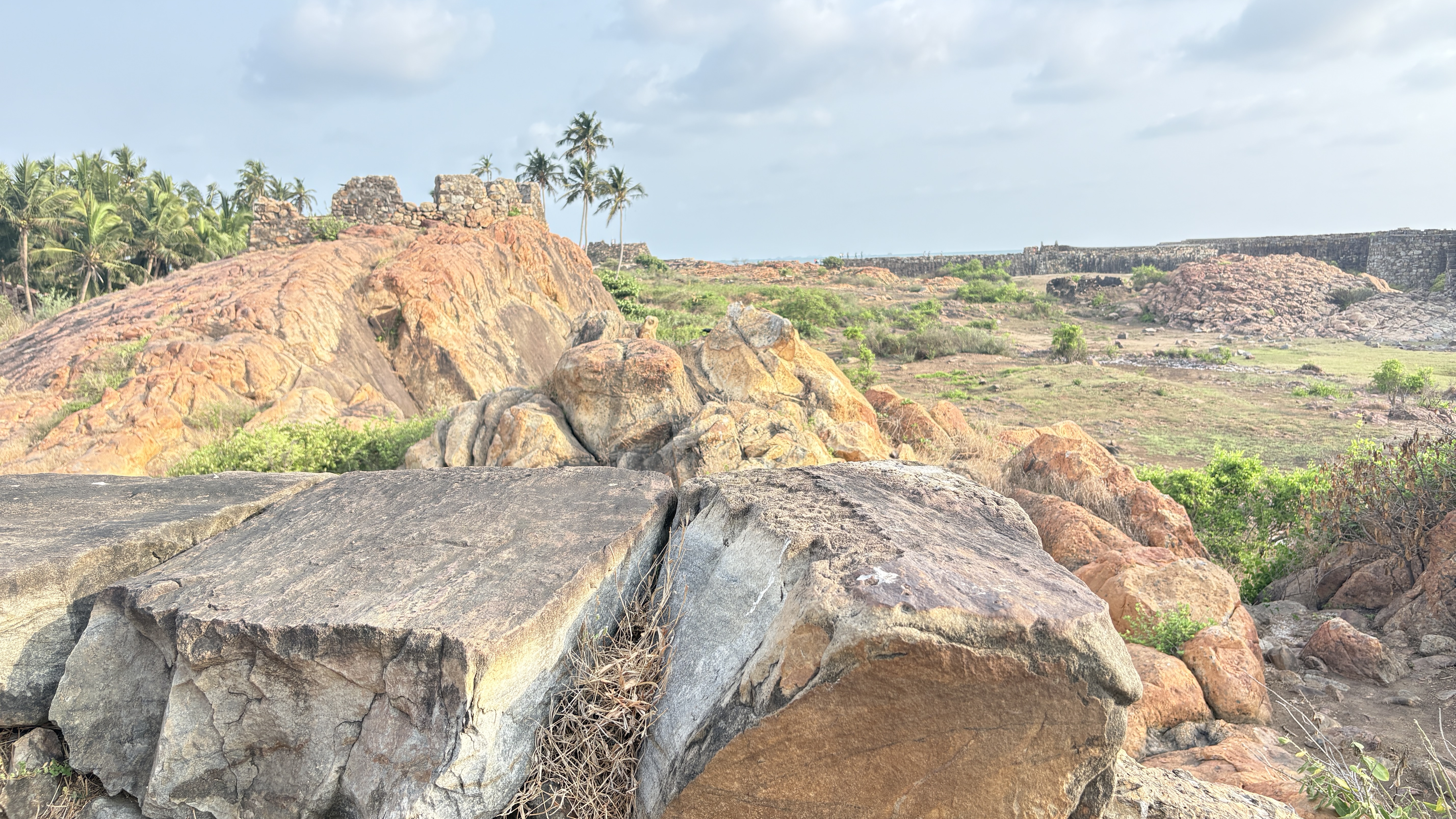 A landscape featuring large, weathered rocks in the foreground, with a hillside of reddish-brown terrain behind.