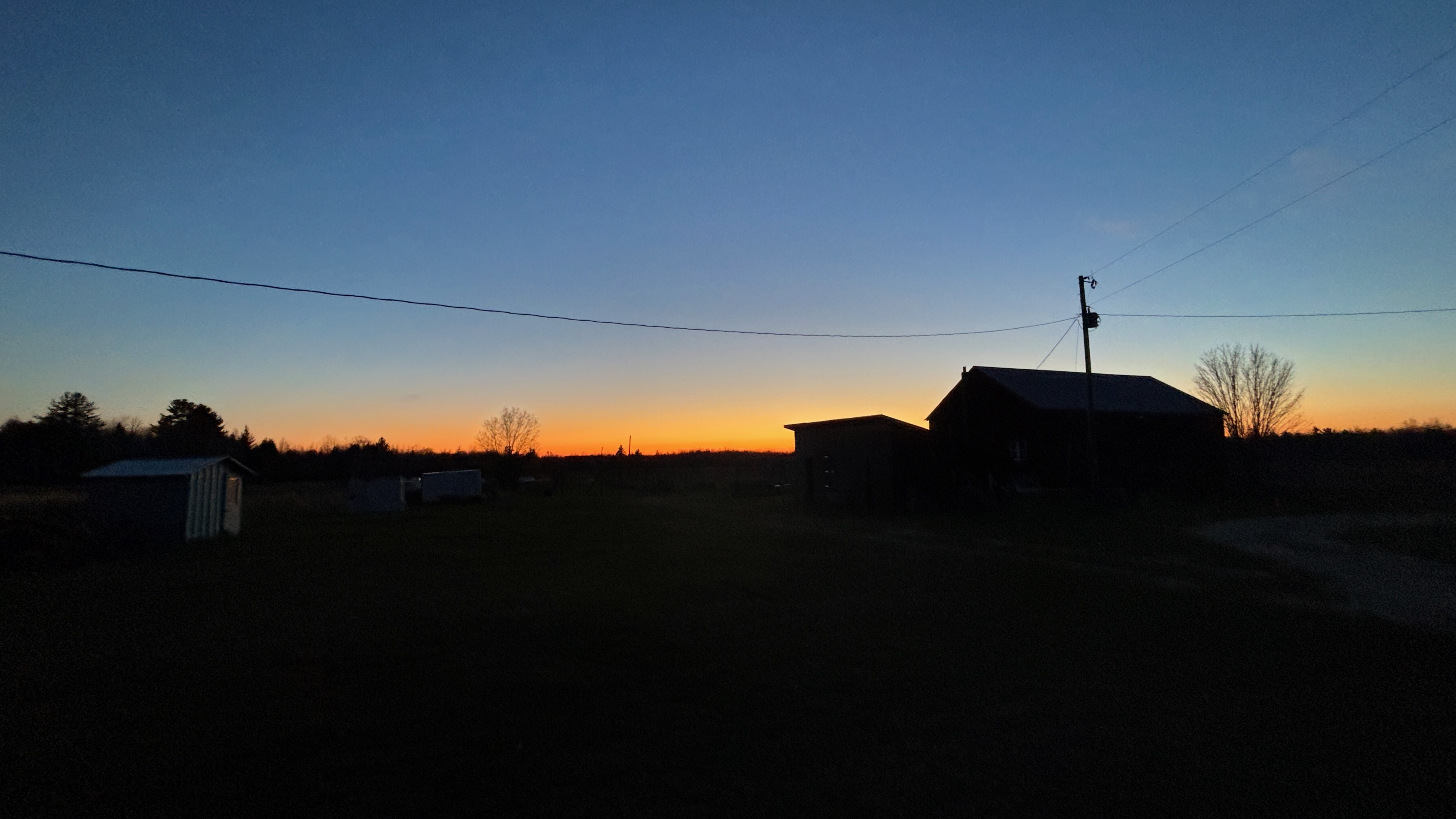An evening sky with the glow of the setting sun on the horizon. Silhouetted are a barn and some other farm buildings.