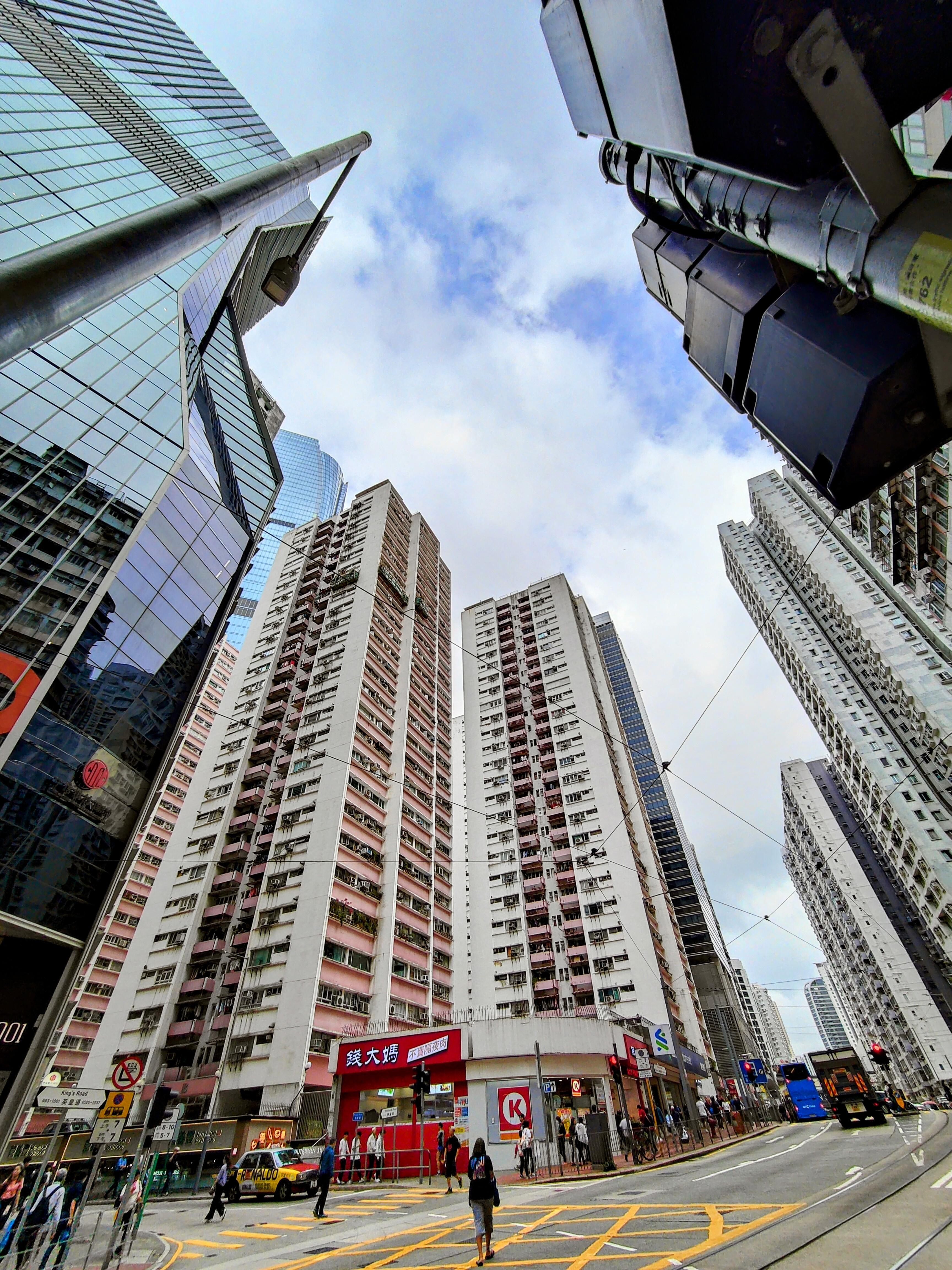 Bustling Hong Kong street scene with towering high-rises, busy crosswalks, and a convenience store at the corner - urban energy at its peak.