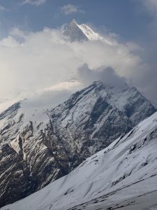A breathtaking view of a snow-covered mountain range under a partly cloudy sky. 