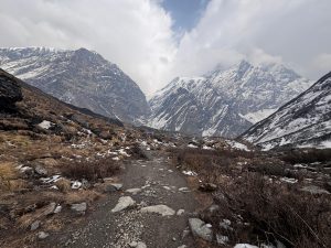 A rocky path winding through a mountainous landscape, with steep, snow-capped peaks in the background.