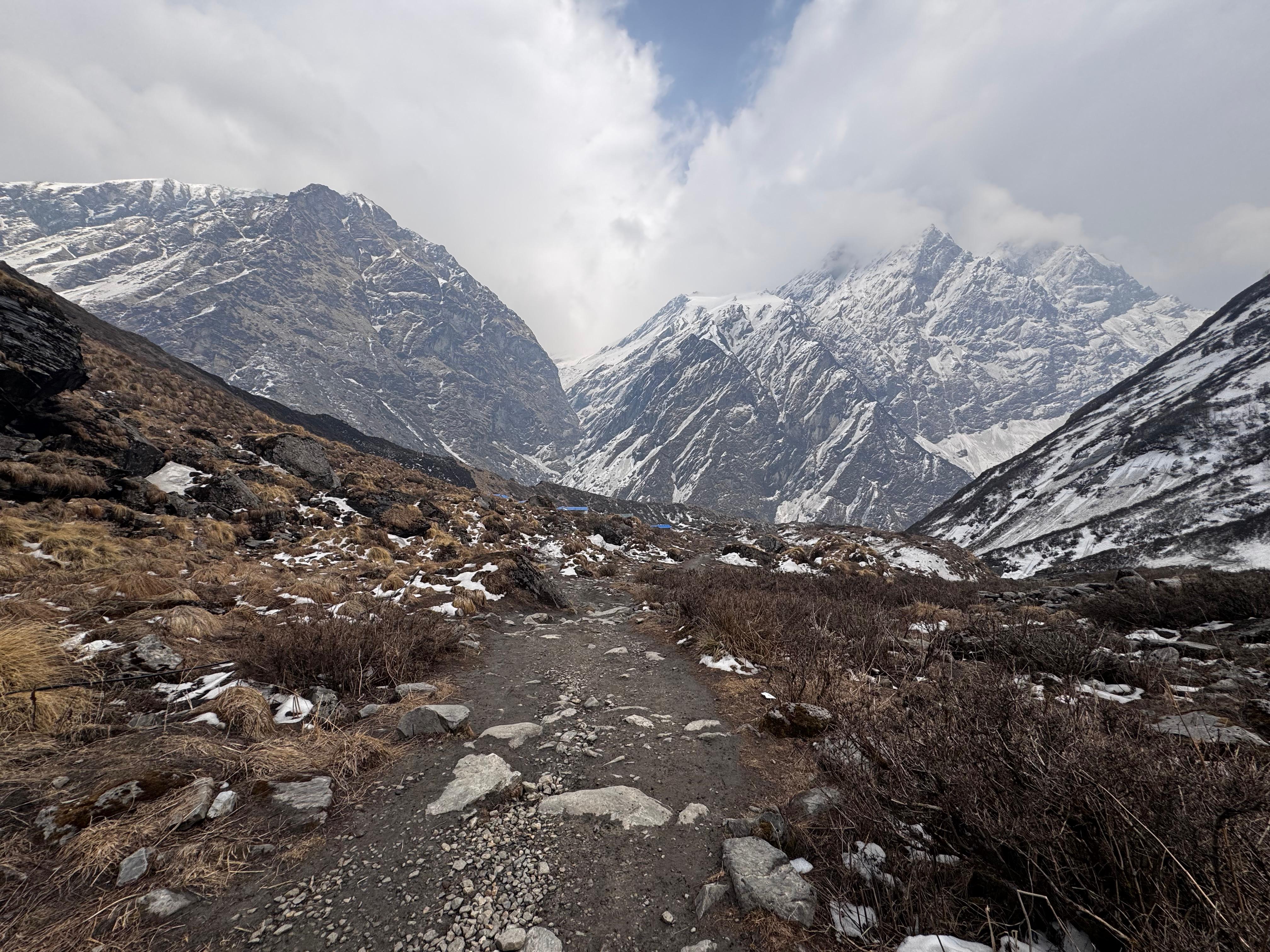 A rocky path winding through a mountainous landscape, with steep, snow-capped peaks in the background.