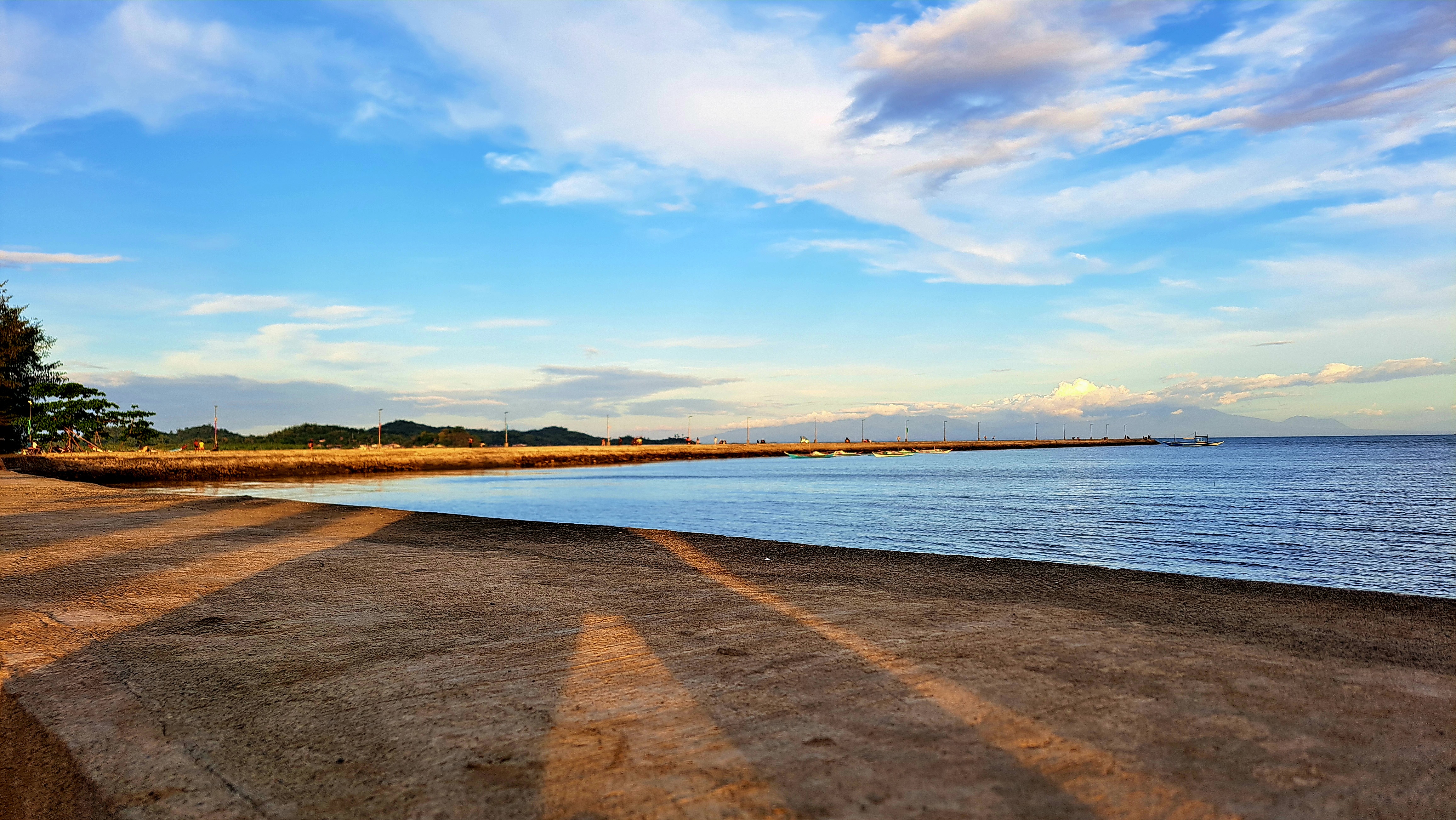 A tranquil beach scene featuring a sandy shore leading to calm waters, with a pier visible in the distance.
