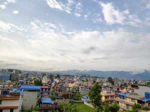 A panoramic view of a colorful urban landscape, featuring a dense arrangement of buildings with various roof colors including blue, red, and gray. 