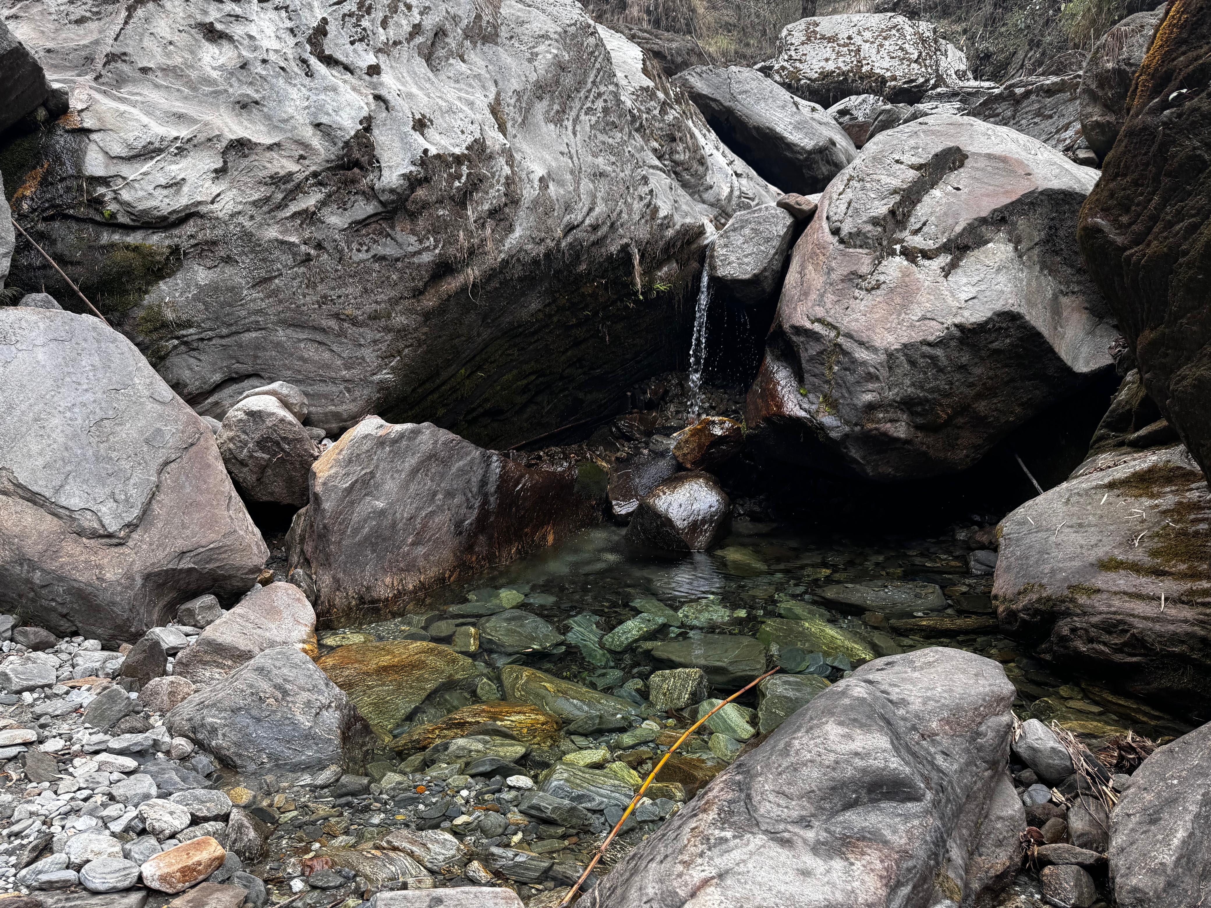 A rocky landscape featuring large boulders of various shapes and sizes arranged around a clear, shallow pool of water.
