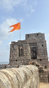 A stone fortification with a decrepit structure is depicted, featuring a prominent orange flag waving atop it.
